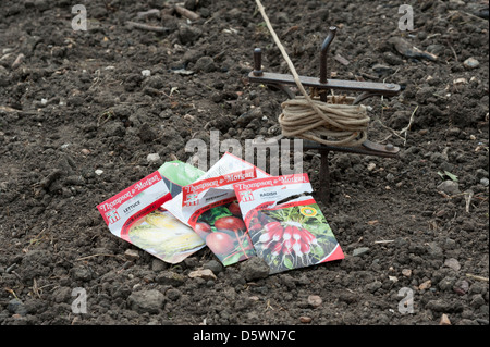 Pakete von Gemüsesamen, liegend auf dem Boden in einem Gemüsegarten bereit für die Bepflanzung. Zeigt Markierungslinie und einem Bohrer hinter. Stockfoto