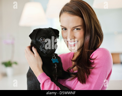 Lächelnde Frau Holding Hund drinnen Stockfoto