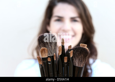 Glückliche junge Frau zeigt eine Vielzahl von Make-up Pinsel Stockfoto