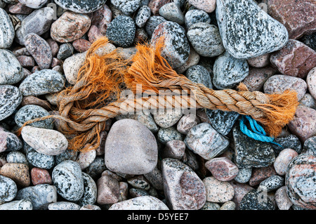 Ein Stück ausgefranste Seil an einem steinigen Strand angespült. Stockfoto