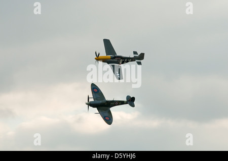 Zwei "Zweiter Weltkrieg" Kampfflugzeuge (Mustang und Spitfire) fliegen in Formation gegen grauen bewölktem Himmel. Stockfoto