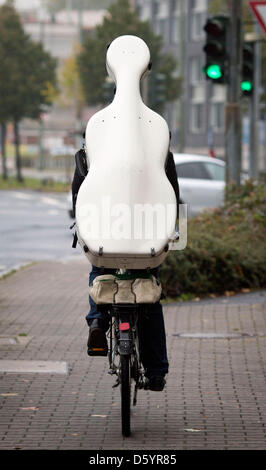 Ein Radfahrer trägt das Gehäuse von einem Saiteninstrument auf seinem Rücken, als er auf seinem Fahrrad durch die Straßen von Frankfurt, Deutschland, 12. Oktober 2012 reitet. Foto: Frank Rumpenhorst Stockfoto