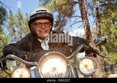 Ältere Mann mit Helm schiefen Motorrad Lenker im Wald Stockfoto