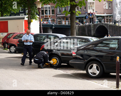 zwei Parkwächter beschäftigt Anbringen eines Wheelclamp am Prinsengracht Kanal, Amsterdam Niederlande Stockfoto