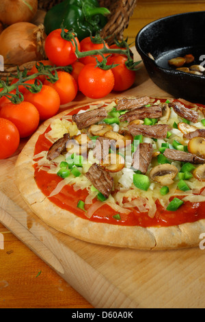 Rindfleisch Champignons und Mozerella Pizza auf einem hölzernen Steckbrett mit Cherry Strauchtomaten, Zwiebeln im Weidenkorb und schwarze Pfanne Stockfoto