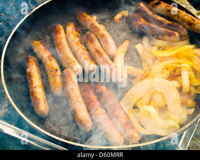 Würstchen und Zwiebeln Braten in der Pfanne auf Einweg-Grill Stockfoto