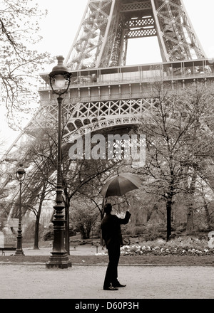 Ein Mann hält einen Regenschirm in der Nähe des Eiffelturms, Paris Frankreich. Stockfoto