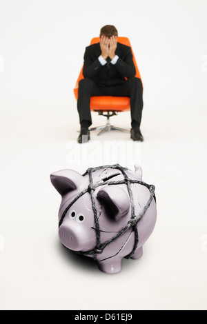 Besorgt Geschäftsmann Stuhl Sparschwein mit einem Seil aus finanziellen Schwierigkeiten gefesselt Stockfoto