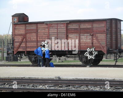 Menschen stehen in der Nähe von Blumen in Form von den Davidstern an einem Güterwagen an der Stelle des ehemaligen deutschen Nazi-Tod Lager Birkenau, in Birkenau, Polen, 19. April 2012. Mehrere tausend Menschen nahmen Teil der jährlichen Holocaust-Gedenken "Marsch der lebenden" auf der Website von der Kriegszeit Nazi-Tod Lager Auschwitz-Birkenau von Oswiecim (Auschwitzt) in Brzezinka (Birkenau). Stockfoto