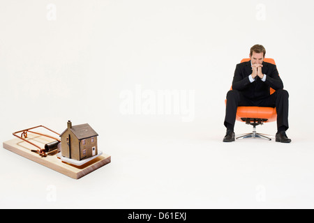 Modell nach Hause Mausefalle mit besorgt Geschäftsmann sitzen Stuhl aus steigenden Immobilien-Preise Stockfoto