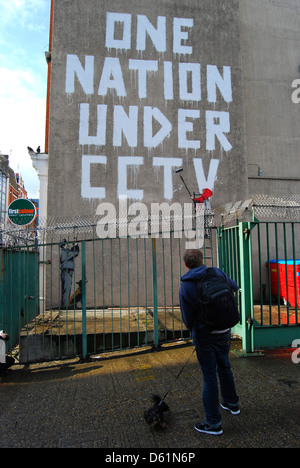 Ein Mann mit seinem Hund befasst sich mit der Arbeit von Banksy in Newman Street, London, UK. Stockfoto