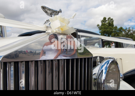 Horizontale Nahaufnahme der Geist der Ekstase Statue und Reflexion einer Braut und Brautjungfern im Grill eines Rolls Royce Oldtimer bei einer Hochzeit. Stockfoto