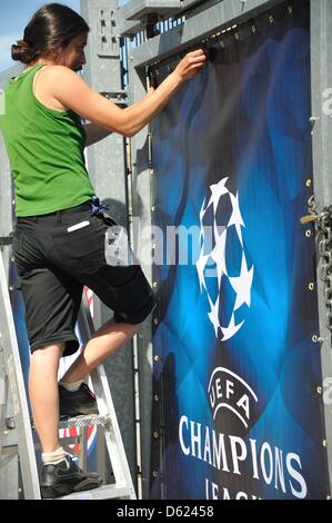 Eine Frau hängt ein blaues Schild mit der Aufschrift "UEFA Champions League - Finale 2012 München" im Eingangsbereich des Stadions für das Endspiel der Champions League in der Allianz Arena in München, Deutschland, 11. Mai 2012. FC Bayern München spielen FC Chelsea im Finale in München am 19. Mai 2012. Foto: Nicolas Armer Stockfoto