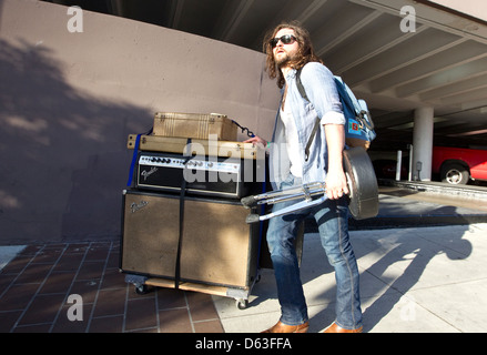 Weiße männliche Musiker schiebt seinen Verstärker auf einem Bürgersteig beim SXSW Festival in Austin, Texas Stockfoto