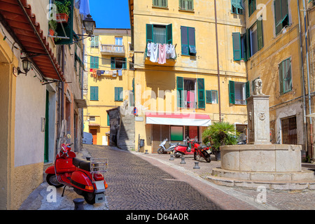 Typische Ansicht der kleine gepflasterte Straße mit Roller unter alten bunten Wohngebäude in der Stadt von Ventimiglia, Italien. Stockfoto