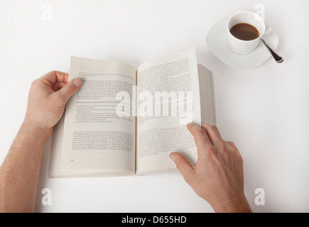 Ein männlicher Student liest in einem Buch, mit einer Tasse Kaffee Stockfoto