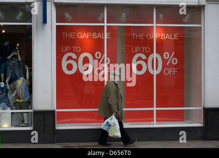 älterer Mann in Tuch Kappe geht einen Zweig der Lücke, wo ein Schaufenster Verkauf Ermäßigungen von bis zu 60 Prozent wirbt Stockfoto