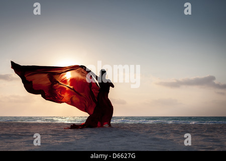 Silhouette einer jungen Frau mit Kopftuch am Strand bei Sonnenaufgang Stockfoto