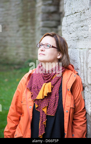 Mit einem ruhigen, verließ Frau outdoor, Neigung zu eine Steinmauer auf Kamera Ausdruck zu betrachten. Stockfoto