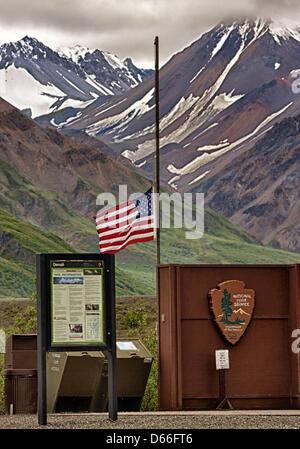 27. Juni 2012 - Denali Borough, Alaska, steht uns - ein schwarzes Brett mit Informationen für Wanderer und Touristen neben dem National Park Service Arrowhead-Logo an der Toklat River Ranger Station im Denali Nationalpark & zu bewahren. Die US-Flagge weht auf Halbmast zu Ehren des Park-Service-Personal, die Kampf gegen Waldbrände gestorben. Schroffe Berge der Alaska Range steigen im Hintergrund. (Kredit-Bild: © Arnold Drapkin/ZUMAPRESS.com) Stockfoto