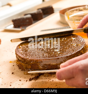 Händen der Koch in Aktion verbreiten Kuchen mit Marmelade Stockfoto