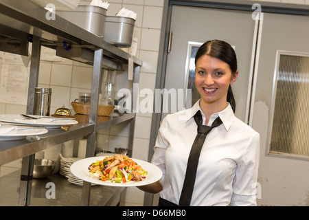 Lächelnd Kellnerin serviert Salat auf Teller in der Küche des Restaurants Stockfoto