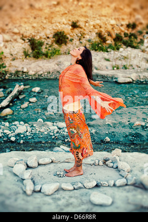 Frau im Freien in der Nähe eines Flusses mit ihren Armen und Herzen öffnen in ein Mandala aus Steinen. Stockfoto