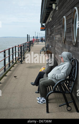 Paar mittleren Alters am Ende des Southend Pier auf einer Bank sitzen und die Vögel mit Brot füttern, an einem grauen windigen Tag. Stockfoto