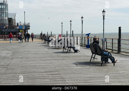 Menschen sitzen auf Bänken am Ende der weltweit längste Vergnügen Pier in Southend, Essex, an einem sonnigen, aber windigen Frühlingstag. Stockfoto