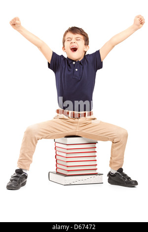 Glückliche Schüler hob seine Hände gestikulieren Glück, sitzend auf einem Stapel Bücher auf weißen Hintergrund Stockfoto