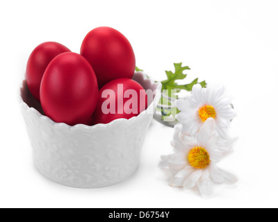 eine Porzellanschüssel voll von roten Ostereier mit einer Blumendekoration auf weißem Hintergrund Stockfoto