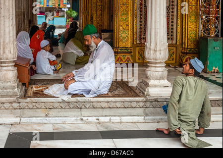 Ein Mann mit grünem Hut betet zwar deaktiviert, Bettler Almosen in Moschee in Nizamuddin, Alt-Delhi, Delhi, Indien geduldig wartet. Stockfoto