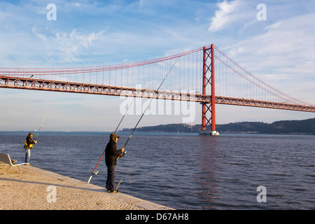 Lissabon, Portugal. Fischer an der Seite des Tejo, die 25 de Abril Brücke im Hintergrund. Stockfoto