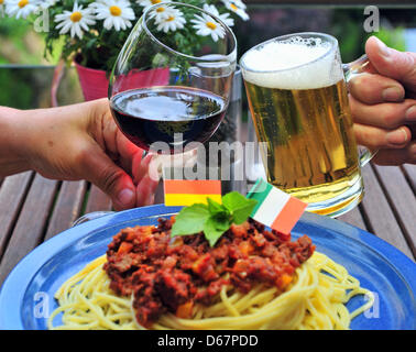 ILLUSTRATION - eine illustrierte Bild zeigt einen Mann und eine Frau, die klirrende Gläser italienischer Rotwein und deutsches Bier auf dem Balkon in Chemnitz, Deutschland, 26. Juni 2012. Ein Teller Spaghetti mit deutschen und italienischen Flagge geschmückt steht im Vordergrund. Deutschland spielen Italien im Halbfinale der EURO 2012 am 28. Juni 2012. Foto: Hendrik Schmidt Stockfoto