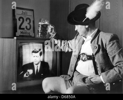 (Dpa Datei) - eine Archiv-Bild vom 23. Juli 2012, zeigt einen bayerischen Mann in traditioneller Kleidung Jubel bei einem Glas Bier beim Ansehen einer live-Übertragung von US-Präsident John F. Kennedy bei einer im Fernsehen übertragenen Rede auf seinem Fernseher in seinem Haus in Bayern, Deutschland, 23. Juli 1962. Der zivile Kommunikationssatellit Telstar wurde am 10 Juli 196 von Cape Canaveral aus gestartet. Stockfoto