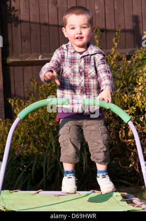 3 Jahre alter Junge mit kurzen Haaren, hüpfen auf einem Trampolin Garten Stockfoto