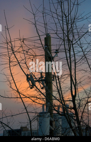 Strommast mit Stromleitungen und Verteilungstransformatoren in den Sonnenuntergang. Stockfoto