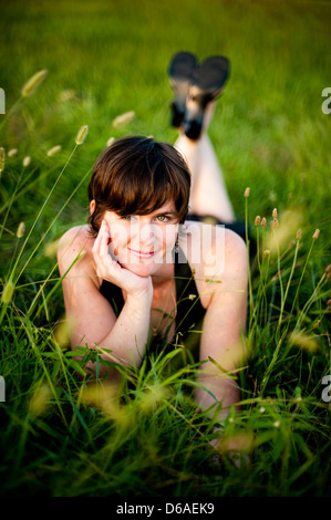 Lächelnde junge Frau, die im Feld liegen Stockfoto