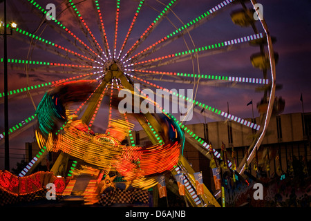 Ausgliederung, ein Fahrgeschäft in der Nacht mit Riesenrad dahinter, fotografiert in der Nacht mit langen Belichtungszeiten zeigen Bewegung verwischen Stockfoto