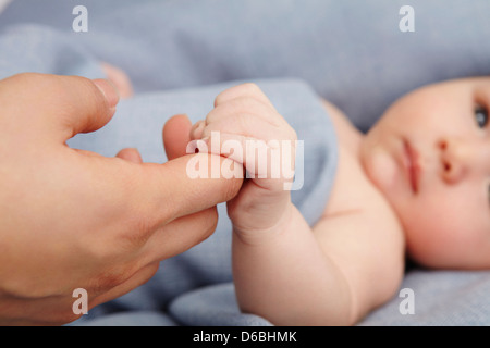 Baby Boy mit Müttern Finger im Bett Stockfoto