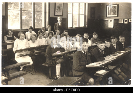 Postkarte von einem Lehrer mit Juniorinnen & Jungs sitzen an ihrem Schreibtisch, mit offenen Bücher im Klassenzimmer, 1940er Jahre, U.K Stockfoto