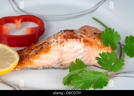 Gegrillter Lachs auf einem Teller mit einer Scheibe Zitrone, roter Pfeffer und Koriander Blätter Stockfoto