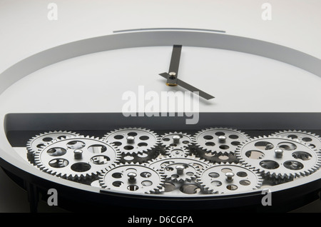 Weiße moderne aussehende Uhr mit schwarzen Händen und Zahnräder drin ist niedriger halb die machen die Uhr ticken. Stockfoto