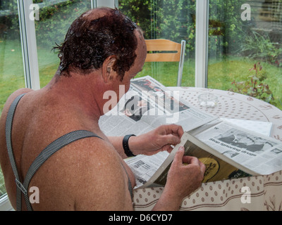 Im mittleren Alter Mann liest Zeitung beim Haare färben ist seine Haare färben. Tragen Zahnspangen, im Wintergarten sitzen. Stockfoto