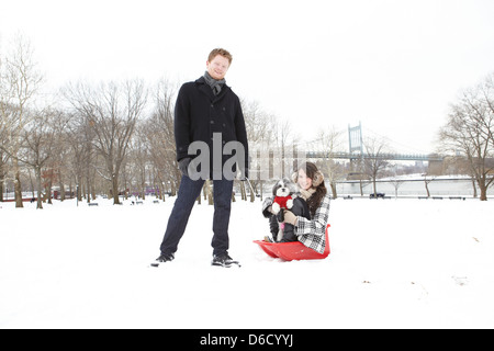 Kerl stehen neben einem Mädchen und Hund sitzen in einem roten Schnee Schlitten im park Stockfoto