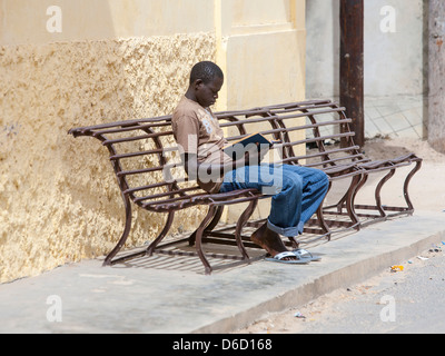 Ein junger Mann afrikanischen sitzen auf einer Bank, einem Bood lesen Stockfoto