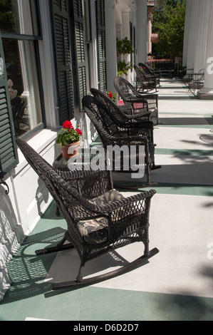 Foto von schwarze Korbweide Schaukelstühle auf große, geräumige südliche Veranda mit Töpfen von Geranien auf kleinen Tischen. Stockfoto