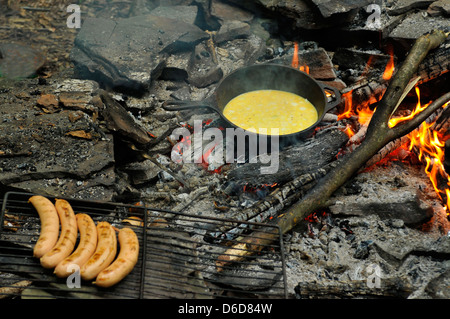 Spiegeleier auf Feuer auf gebratenen Eisenpfanne mit gegrillten Würstchen am Spieß Stockfoto