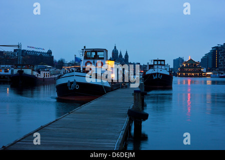 Hafen von Amsterdam Oosterdok vor Sonnenaufgang mit der St.-Nikolaus-Kirche im Hintergrund. Stockfoto