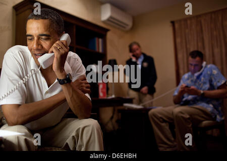 US-Präsident Barack Obama telefoniert, 10 amerikanische Militärangehörige stationiert auf der ganzen Welt, von seinem Urlaub Vermietung Haus in Kailua, Hawaii, 24. Dezember 2011. White House Communications Agency (WHCA) Presidential Communications Officer CPT Mallory Fritz und Military Aide Oberstleutnant Sam Price koordinieren die Anrufe im Hintergrund. Obligatorische Credit: Pe Stockfoto